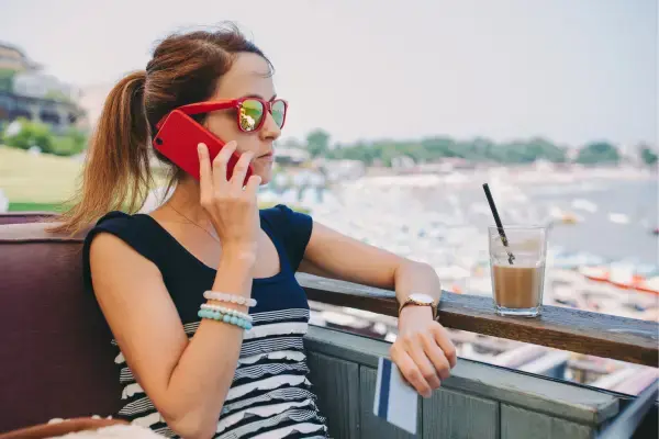 Mulher falando ao celular em viagem segurando cartão de crédito (Fonte: Canva)