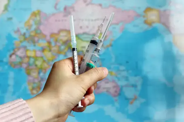 Mão segurando seringas em frente a um mapa mundi (Fonte: Adobe Stock)