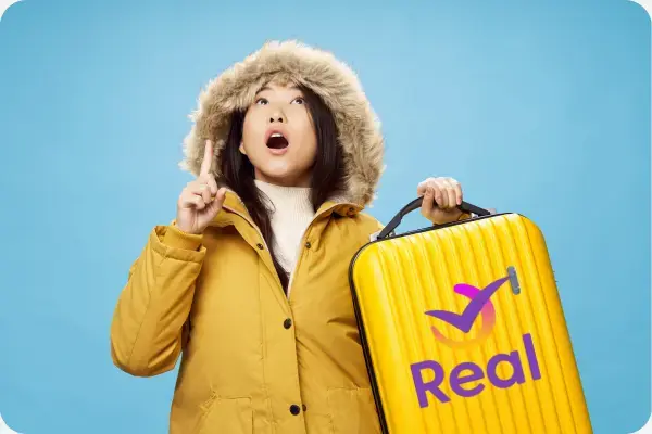 Imagem de uma mulher com roupas de frio e segurando uma mala.