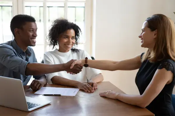 Mulher apertando a mão de um homem após fechar negócio com casal (Fonte: Canva)