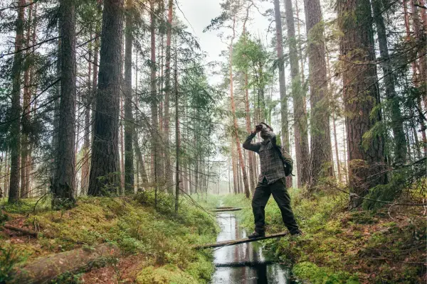 Homem em floresta observando com um binóculo as árvores e animais