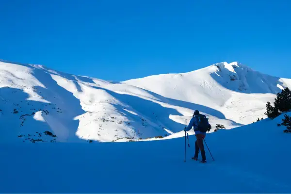 Pessoa praticando caminhada na neve nos Alpes italianos com bastões e mochila durante o inverno europeu.