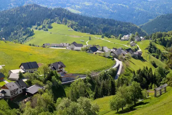 Vilarejo com casas espalhadas entre colinas verdes e montanhas ao fundo.
