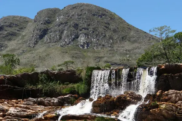 Cachoeira sobre rochas na Serra do Cipó com montanhas e céu azul ao fundo