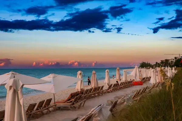 Espreguiçadeiras e guarda-sóis fechados em praia caribenha ao pôr do sol