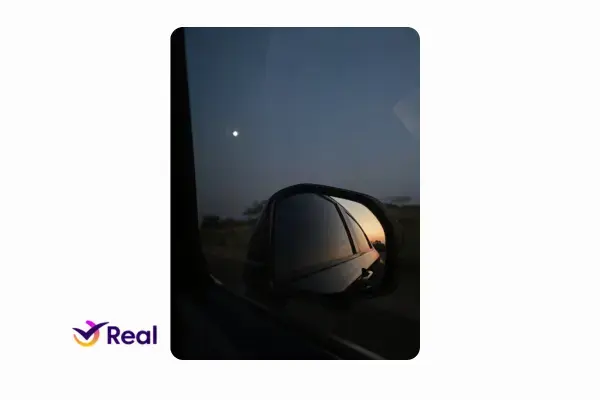 imagem do sol nascendo, mas o céu ainda escuro. ponto de vista de alguem dentro doc arro, observando o retrovisor com o reflexo do sol nascente.