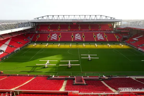 Anfield Stadium vazio com arquibancadas vermelhas e sistema de irrigação no gramado.