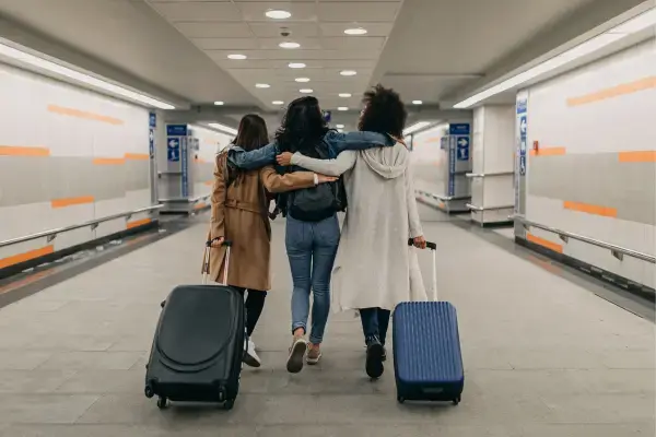 Amigas, puxando malas, andando abraçadas em aeroporto