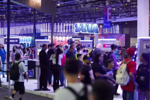 Imagem da BGS com estande da SEGA ao fundo, cercado por visitantes testando jogos e explorando o evento.