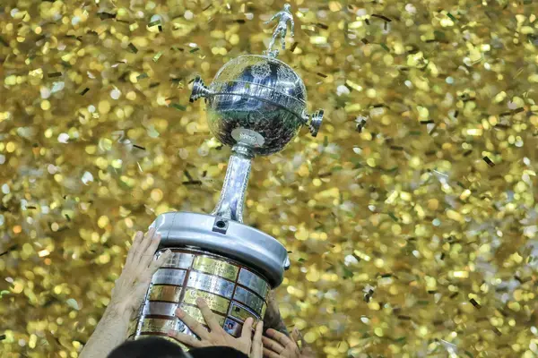 Close do troféu da Copa Libertadores da América sendo erguido sob uma chuva de confetes dourados.