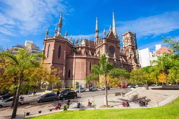 Imagem da catedral de Córdoba, um monumento impressionante em estilo gótico localizado na cidade, cercada por árvores e estacionamento, com céu azul ao fundo.