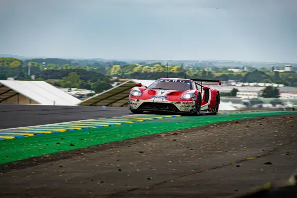 Ford GT de corrida contornando curva do Circuit de la Sarthe durante as 24 Horas de Le Mans, com área verde e zebras coloridas na pista.