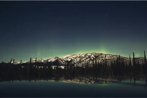 Aurora boreal verde refletida em lago com montanhas nevadas no Jasper, Canadá