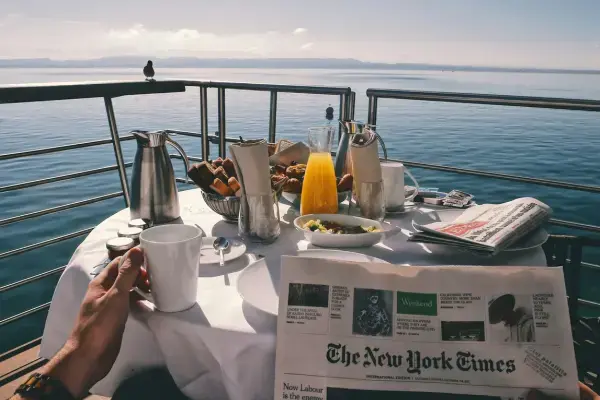 Café da manhã servido em mesa com vista para o mar, com suco, pães e xícara de café