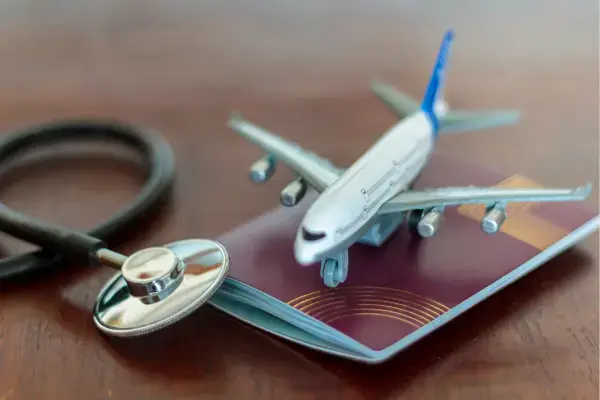 Miniatura de avião sobre passaporte com estetoscópio, simbolizando seguro viagem e cuidados com a saúde.