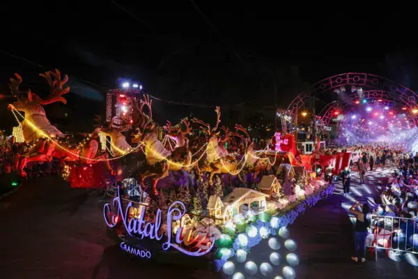 Carro alegórico do Natal Luz de Gramado com renas iluminadas e estrutura cenográfica passando por avenida lotada de espectadores.