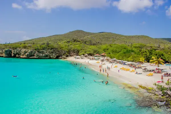 Praia de areia branca e mar turquesa cercada por encosta com cactos em Curaçao
