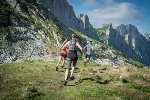 Três corredores de trail running subindo trilha em montanha rochosa