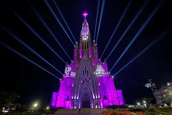 Catedral de Pedra de Canela iluminada com luzes roxas e feixes de luz durante show noturno gratuito