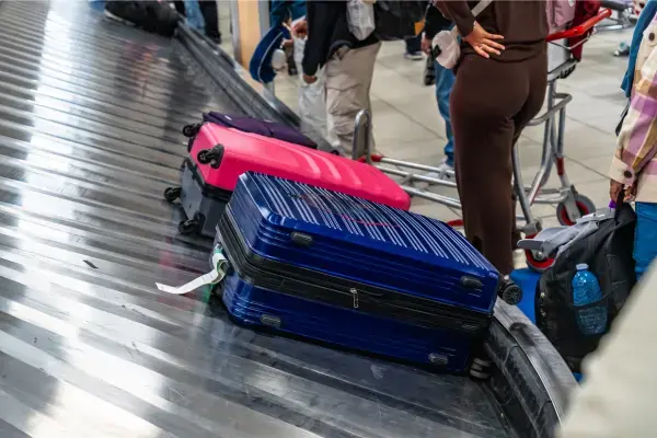 Malas coloridas na esteira de bagagem de um aeroporto com passageiros aguardando