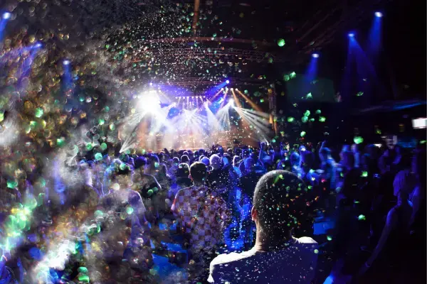 Público dançando em festival de música eletrônica com luzes e confetes coloridos (Fonte: Canva)