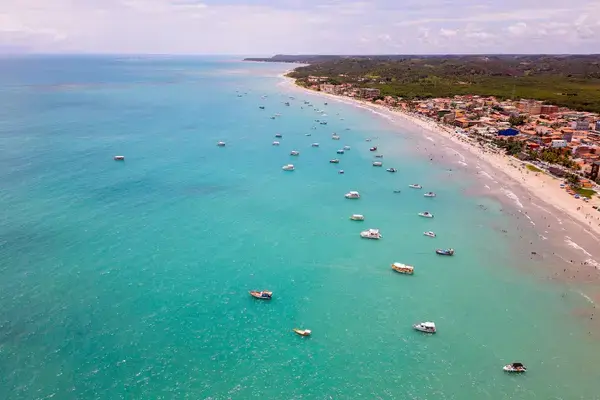 Vista aérea da praia de Maragogi com águas azul-turquesa, barcos e construções na orla.