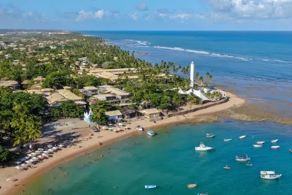 Vista aérea da Praia do Forte com mar calmo, barcos e área urbana integrada à natureza.