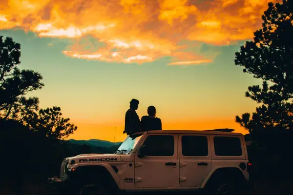 Casal ao lado de um carro observando paisagem ao por do sol