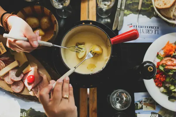 Fondue de queijo com garfos mergulhando na panela e frios ao redor