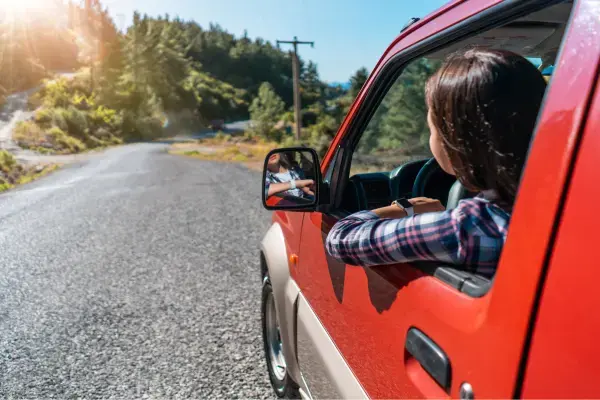 Mulher dirigindo um carro vermelho em estrada arborizada, aproveitando uma road trip.