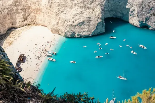 Vista aérea de Navagio Beach, em Zakynthos, com praia cercada por falésias brancas, barcos ancorados e o navio naufragado na areia.