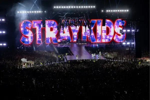 Stray Kids se apresentando no Tottenham Hotspur Stadium com o nome da banda iluminado, diante de multidão em festival internacional.