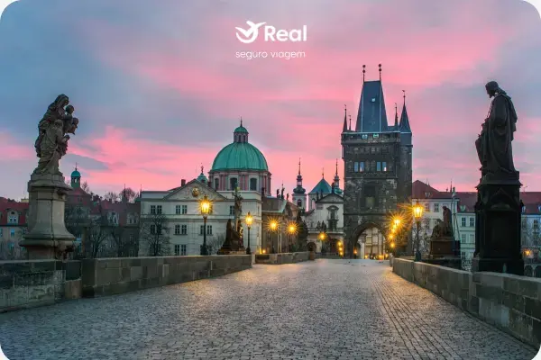 Vista panorâmica da Ponte Carlos em Praga ao amanhecer, com as estátuas em silhueta e o Castelo de Praga ao fundo