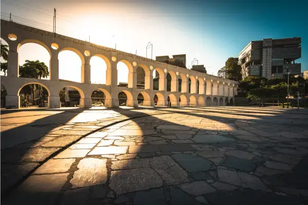 Foto dos Arcos da Lapa no Rio de Janeiro ao entardecer, com luz dourada e sombras projetadas no chão de pedra.