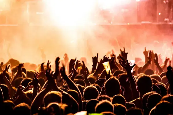 Público em show noturno em São Paulo, com mãos levantadas, copos no ar e iluminação intensa vinda do palco.