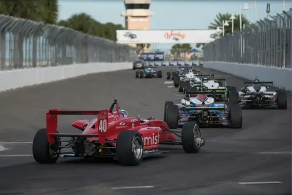 Carros de fórmula alinhados em circuito urbano durante corrida, com arquibancadas e torre de controle ao fundo.