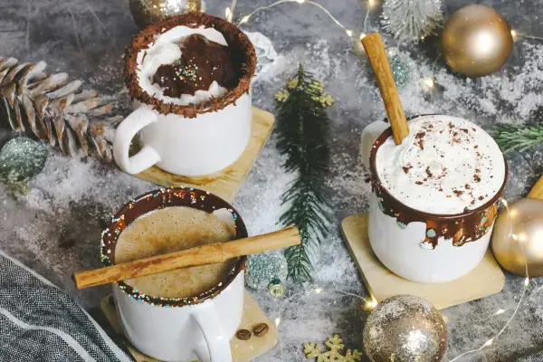 Três canecas de chocolate quente com canela e chantilly.