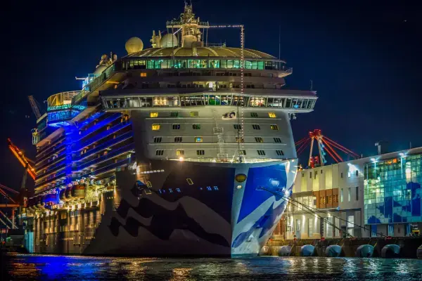Navio de cruzeiro iluminado e atracado no porto durante a noite, visto de frente