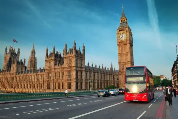 Vista do Palácio de Westminster e do Big Ben ao pôr do sol, com um ônibus vermelho de dois andares passando pela ponte Westminster Bridge em Londres.