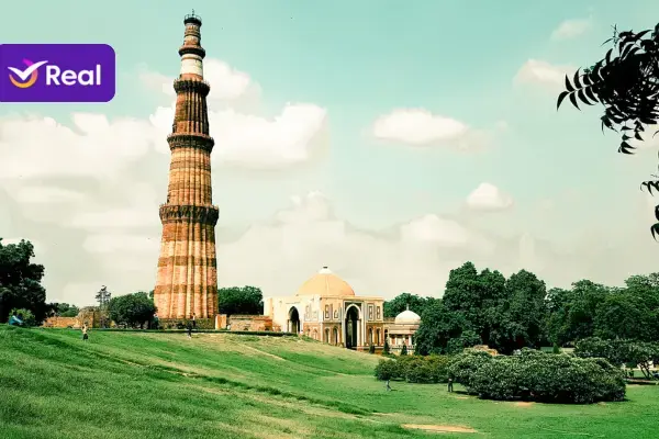 Qutub Minar, uma torre histórica de tijolos, cercada por jardins verdes e céu azul.