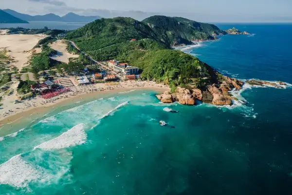 Vista aérea de Laguna em Santa Catarina com mar azul, orla urbanizada e morros verdes ao fundo.