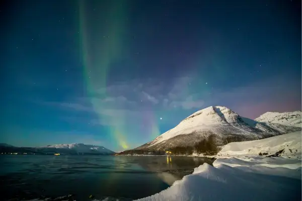 Aurora boreal sobre fiorde e montanhas nevadas em Tromsø, no Ártico norueguês