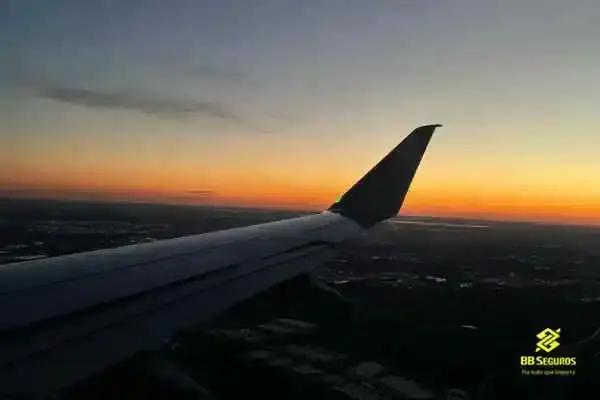Avião voando no pôr do sol e logo da BB Seguros