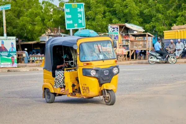 Triciclo motorizado amarelo transportando passageiros em uma estrada movimentada.