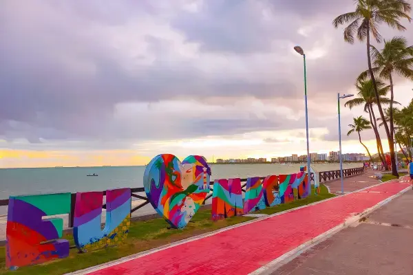 Placa colorida "Eu Amo Maceió" na orla da cidade ao entardecer
