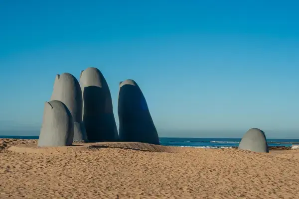 Escultura de mão na areia de praia, no Uruguai