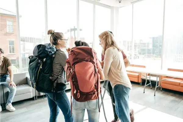 Grupo de viajantes com mochilas grandes em área de espera iluminada, prontos para seguir viagem.
