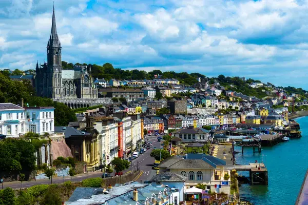 Paisagem de uma cidade costeira com casas coloridas, igreja no topo da colina e porto movimentado em dia ensolarado.
