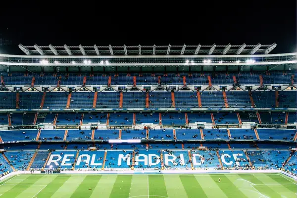 Vista interna do estádio Santiago Bernabéu em Madri, com arquibancadas azuis e o nome Real Madrid CF em destaque no setor central.