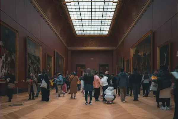 Visitantes observam grandes pinturas em galeria de museu europeu com teto de vidro